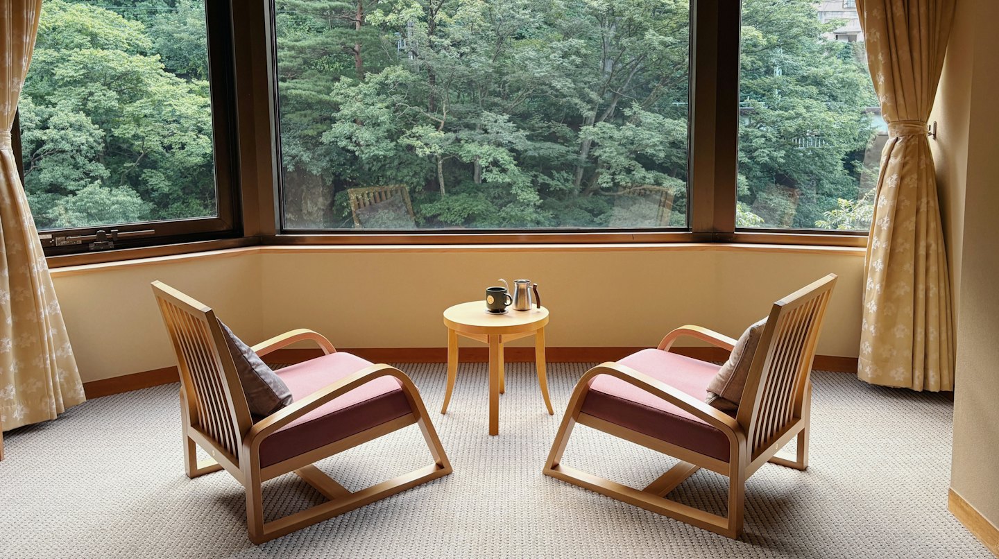 Two chairs and a table sit before a forest view.